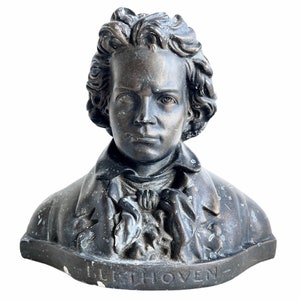 Può includere: Un busto in bronzo di un giovane Beethoven. La scultura è dettagliata e mostra il viso e la parte superiore del busto del compositore. La base della scultura è incisa con il nome "BEETHOVEN".
