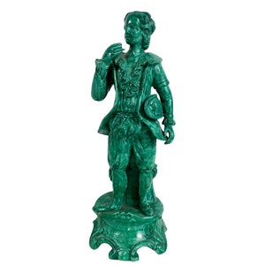 May include: A green ceramic statue of a man in a 17th-century style outfit, standing on a decorative base.