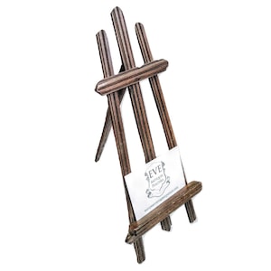 May include: A small wooden easel with a striped design. The easel is holding a business card that reads "Eve Antique Pictures".