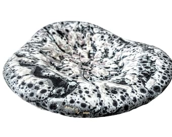 May include: A white ceramic dish with a black and gray speckled pattern. The dish is shaped like a shallow bowl and has a slightly rounded edge.