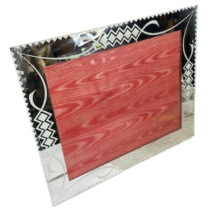 May include: A silver picture frame with a black and white geometric design. The frame has a red velvet backing.