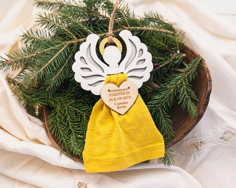 May include: White wooden angel ornament with a yellow fabric pouch and a heart-shaped wooden tag that reads "Forever in our hearts, Grandma Bernie".