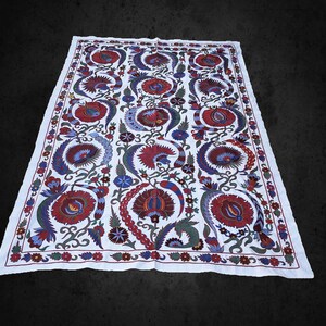 May include: White cotton fabric with a traditional floral embroidery pattern in shades of red, blue, and green. The design features stylized flowers, leaves, and vines.