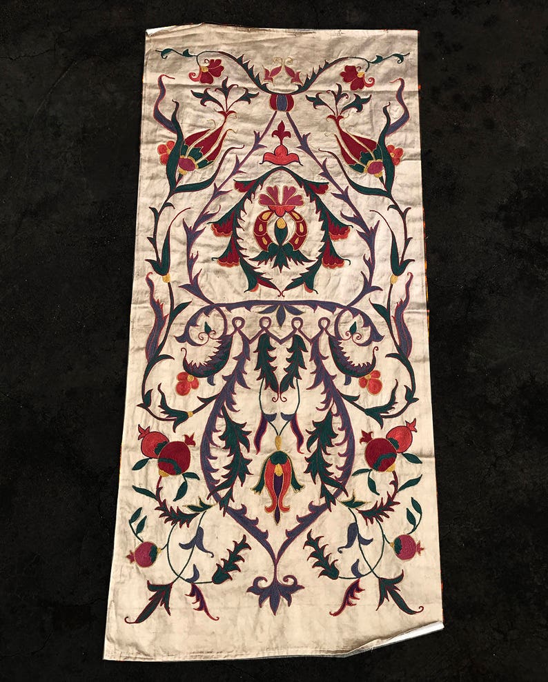 May include: A white fabric panel with a traditional floral design embroidered in shades of red, green, purple, and gold. The design features stylized flowers, leaves, and pomegranates.