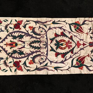 May include: A white fabric panel with an intricate embroidered design featuring stylized flowers, leaves, and pomegranates in shades of red, green, purple, and gold.