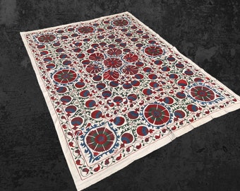 Puede incluir: Tela blanca con bordado intrincado con motivos florales rojos, azules y verdes. El diseño incluye flores y hojas estilizadas, creando un aspecto tradicional y elegante.