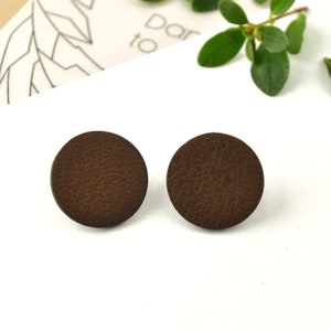May include: A pair of brown leather stud earrings. The earrings are round and have a textured surface.