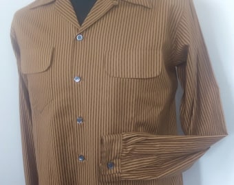 May include: A brown button-down shirt with vertical stripes and two chest pockets. The long-sleeved shirt has a classic collar and buttoned cuffs. The shirt is displayed on a mannequin.