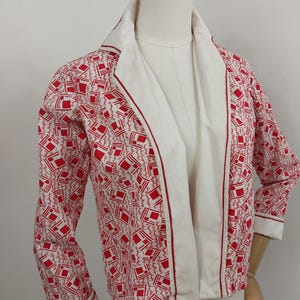 May include: A white and red patterned jacket with a long sleeve and a collar. The jacket has a red trim around the edges and a white lining.