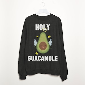 Könnte beinhalten: Ein schwarzer Langarmsweatshirt mit dem Text "HOLY GUACAMOLE" in Weiß. Ein Cartoon-Avocado mit Heiligenschein und Flügeln befindet sich in der Mitte des Textes.