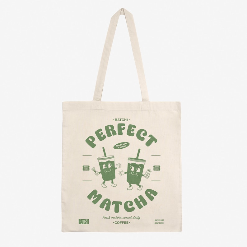 Peut inclure: Un sac fourre-tout en toile blanche avec du texte et des illustrations verts. Le texte indique "BATCHI" "PERFECT" "MATCHA" "Fresh matcha served daily" "BATCHI" "COFFEE". L'illustration montre deux tasses de matcha de dessin anim&eacute; avec des visages.