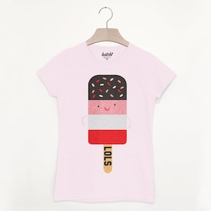 May include: Pink t-shirt with a graphic of a smiling popsicle with chocolate, pink, and white layers and sprinkles. The popsicle stick says "LOLS".