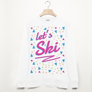 May include: White long-sleeved sweatshirt with a colourful confetti pattern and the text "let's Ski" in pink and blue lettering.