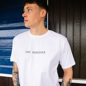 May include: A white t-shirt with the text "SHHH HUNGOVER" printed on the front.