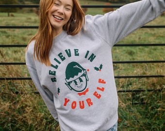 May include: A gray sweatshirt with a green elf graphic and the text "Believe in your elf" in red and white.