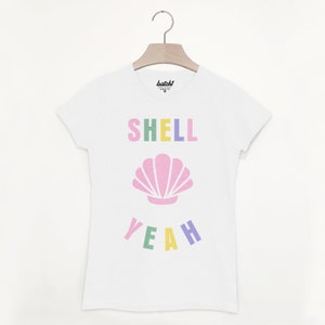 Pu&ograve; includere: Maglietta bianca con una grafica colorata che dice "SHELL YEAH" con una conchiglia rosa al centro.