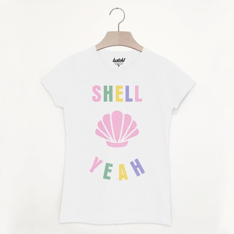 Pu&ograve; includere: Maglietta bianca con una grafica colorata che dice "SHELL YEAH" con una conchiglia rosa al centro.
