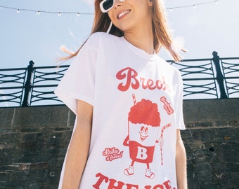 Può includere: Maglietta bianca con una grafica rossa di un personaggio di gelato dei cartoni animati con il testo "Break the Ice" e "Strawberry Swirl" sul davanti.