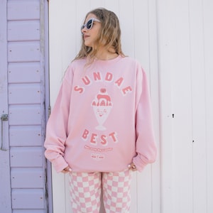 Op de afbeelding: Roze sweatshirt met een afbeelding van een sundae-ijsje met de tekst "SUNDAE BEST" en de zin "Make every day a sundae".