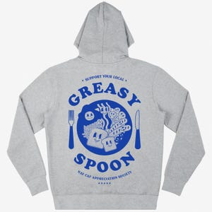 May include: A gray hooded sweatshirt with a blue graphic print on the back. The graphic features a plate of food with a fork and knife, and the text "Support Your Local Greasy Spoon NAF CAF Appreciation Society".