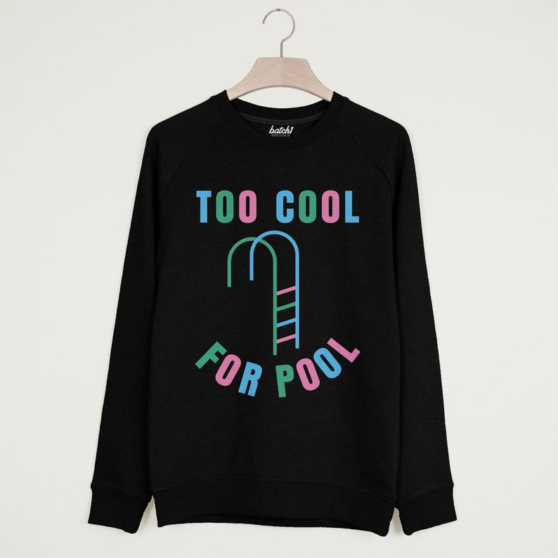 以下が含まれることがあります： カラフルな文字で「TOO COOL FOR POOL」と書かれた黒いスウェットシャツ。 「COOL」と「FOR」の間に、プールのはしごのスタイリッシュな画像があります。
