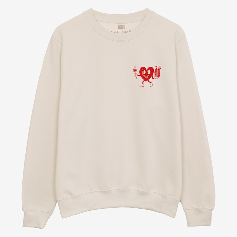 May include: A cream colored sweatshirt with a red heart graphic holding a glass of wine and a stack of books. The text "well done" is printed on the back of the sweatshirt.