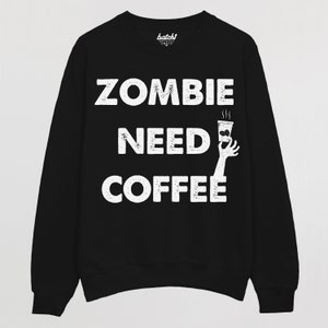 May include: Black sweatshirt with the white text "ZOMBIE NEED COFFEE". A white graphic of a zombie hand holding a coffee cup is also featured. The sweatshirt has a crew neck and long sleeves. The brand name is at the top.