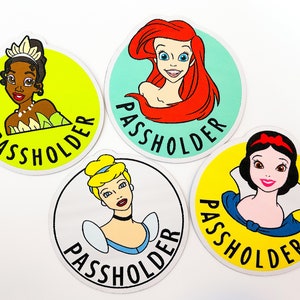 May include: Four round stickers featuring Disney princesses. Each sticker has a yellow, green, blue, or white background with a princess image and the text "Passholder" in black.