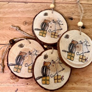 May include: Four wooden ornaments featuring painted images of mice and chipmunks holding presents. The ornaments are round and have a rustic wood grain texture. Each ornament has a twine loop for hanging.
