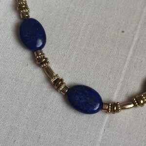 May include: A gold and blue necklace with oval-shaped lapis lazuli stones and gold beads.