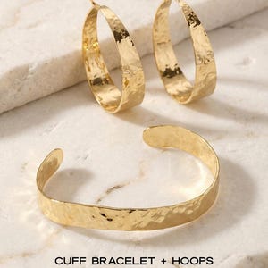 May include: A gold-coloured jewellery set featuring a cuff bracelet and two hoop earrings. The jewellery has a hammered texture. The text on the image reads "CUFF BRACELET + HOOPS STACK SET."