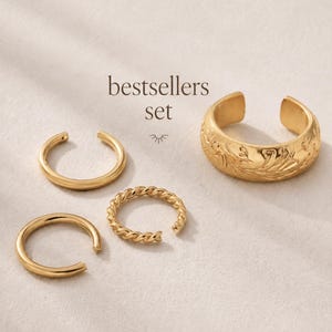May include: A set of four gold-toned ear cuffs labeled "bestsellers set". The collection includes two plain smooth bands, one twisted rope-textured band, and one wider band featuring an embossed floral pattern. Each piece is an open-style ring.