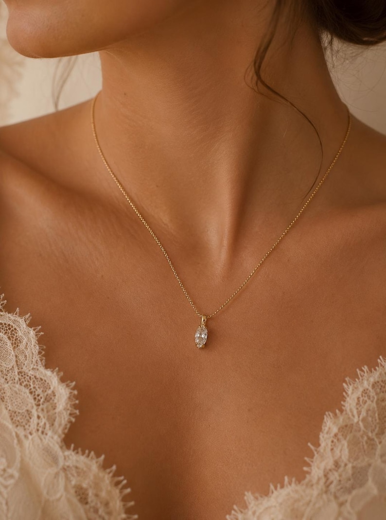May include: A delicate gold necklace featuring a marquise-cut gemstone pendant. The pendant is suspended from a fine chain, creating a simple yet elegant design. The necklace is shown against a skin tone background.
