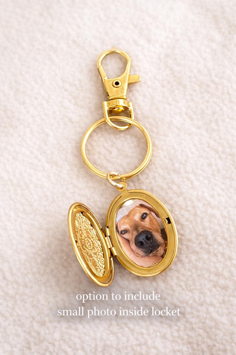 May include: Gold-colored locket keychain with a photo of a dog inside. The locket is oval-shaped and opens to reveal the photo. The keychain has a clasp and a ring. Text on the image reads: "option to include small photo inside locket."