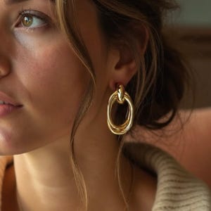 May include: Gold-toned earrings with a triple-loop design. The earrings have a polished finish and a post-back closure. The earrings are a classic accessory, suitable for various occasions.