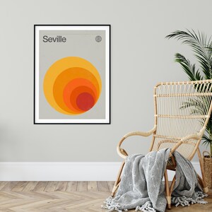 May include: A minimalist poster with the word "Seville" in black text at the top. A stylized graphic of concentric circles in shades of orange, yellow, and red is centered on the poster.