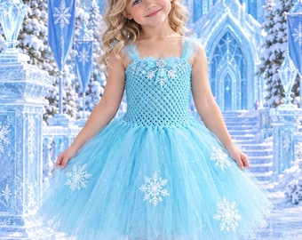 May include: A light blue sleeveless dress featuring a crocheted bodice with a central snowflake embellishment and a layered tulle skirt adorned with white snowflake appliques and subtle glitter accents throughout the fabric.