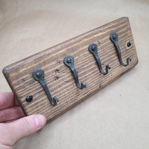 May include: A wooden key rack with four black metal hooks. The rack is made of reclaimed wood and has a rustic finish.