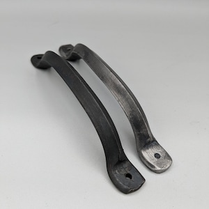 May include: Two black metal cabinet door pulls with a curved design. The pulls have a slightly hammered finish and are approximately 5 inches long.