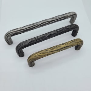 May include: Three metal cabinet pulls with a rustic, wood-like texture. The pulls are in silver, black, and gold finishes.