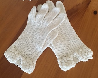 May include: A pair of white crocheted gloves with a ruffled edge. The gloves are made of a delicate, lightweight yarn and have a classic, elegant design.