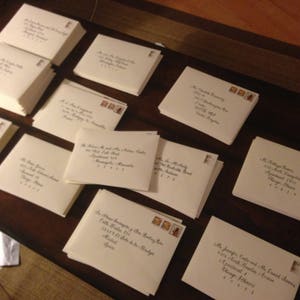 May include: A table top with a stack of white envelopes with black calligraphy and stamps. The envelopes are arranged in rows and columns.