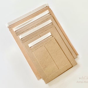 May include: Several brown paper envelopes of different sizes, sealed with white adhesive tape. The envelopes are arranged at an angle, displaying their varying dimensions and the adhesive closure.