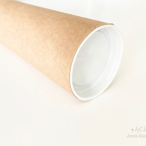 May include: A rolled-up poster or print in a brown cardboard tube with a white interior. The tube is on a white surface. The text "Art by Anna Alvarado" is visible in the lower right corner.