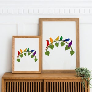 May include: Two framed art prints showing a collection of colourful birds on a leafy branch. The birds are red, orange, yellow, green, blue, and purple. The frames are light brown wood, and the artwork is displayed on a wooden cabinet.