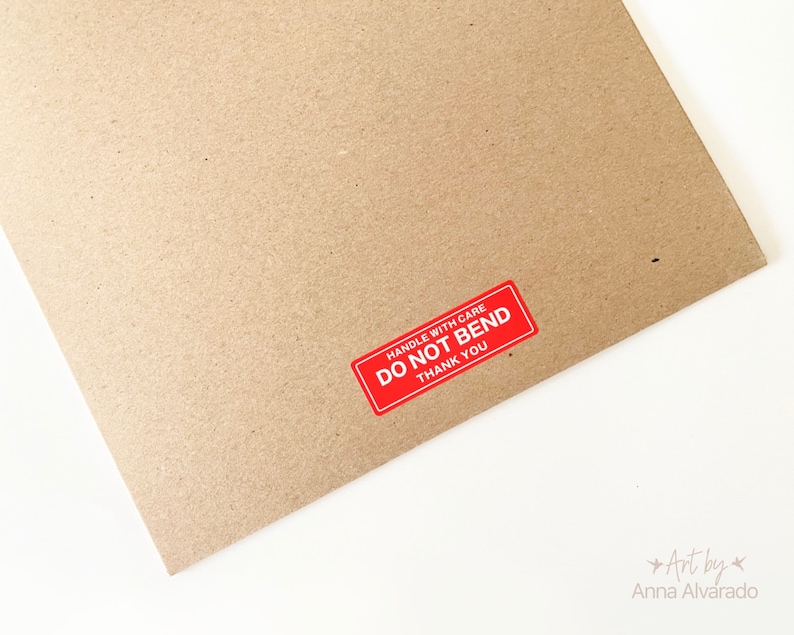 May include: A brown cardboard package with a red sticker that says "HANDLE WITH CARE DO NOT BEND THANK YOU". The package is on a white surface.