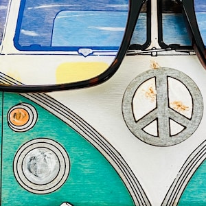 May include: A teal and white vintage Volkswagen bus with a peace sign on the front. The bus is painted with black lines and has a yellow headlight. The bus is reflected in a pair of brown and black eyeglasses.