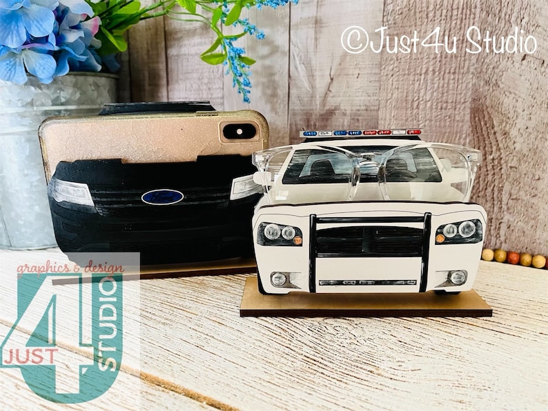 Pu&ograve; includere: Un'auto della polizia bianca con una griglia nera e luci lampeggianti rosse e blu sulla parte superiore. L'auto &egrave; su un supporto in legno con un paio di occhiali in plastica trasparente sopra l'auto. L'auto &egrave; un accessorio per esporre gli occhiali.