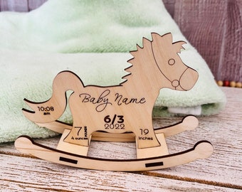 May include: A wooden rocking horse keepsake with a personalized inscription "Baby Name" and the date "6/3/2022". The horse is decorated with a 7 pound, 19 inch measurement scale.