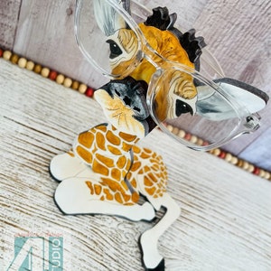 K&ouml;nnte beinhalten: Ein skurriler Brillenhalter in Form einer Giraffe. Der Halter ist mit einem Giraffenmuster in Braun- und Wei&szlig;t&ouml;nen bemalt. Klare Brillen liegen auf dem Halter. Der Text "Just4u Studio" ist sichtbar.